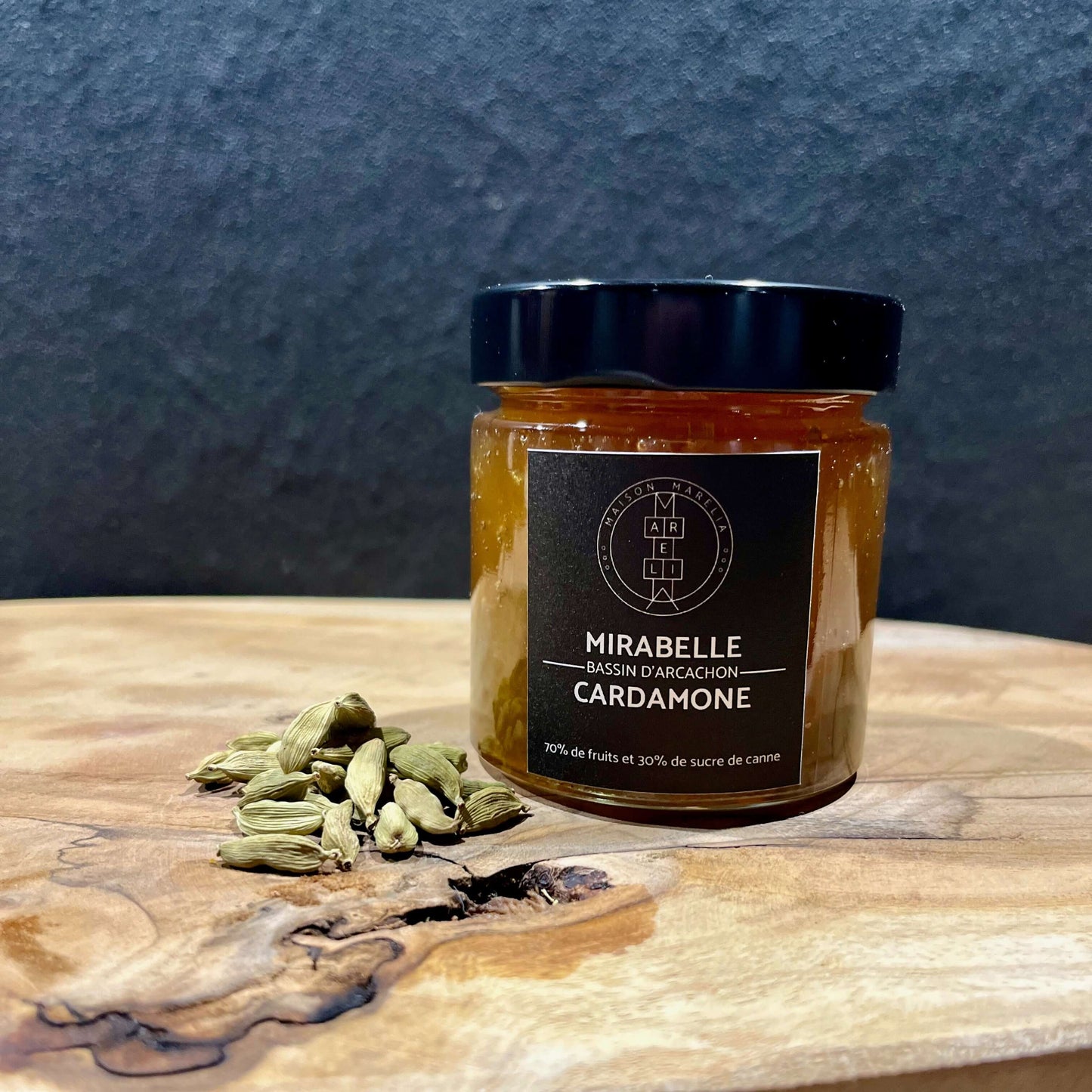 Confiture Mirabelle Cardamone Verte, 70% de fruits 30% de sucre, sur fond bleu et sur une planche en bois accompagné de cardamonne